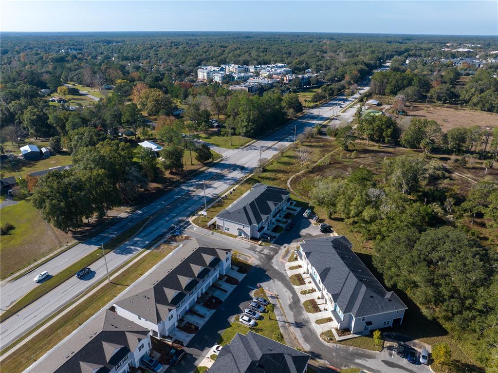 An aerial view shows several modern townhomes situated next to a multi-lane road and forest — 704 NW 126TH TERRACE, NEWBERRY, FL
