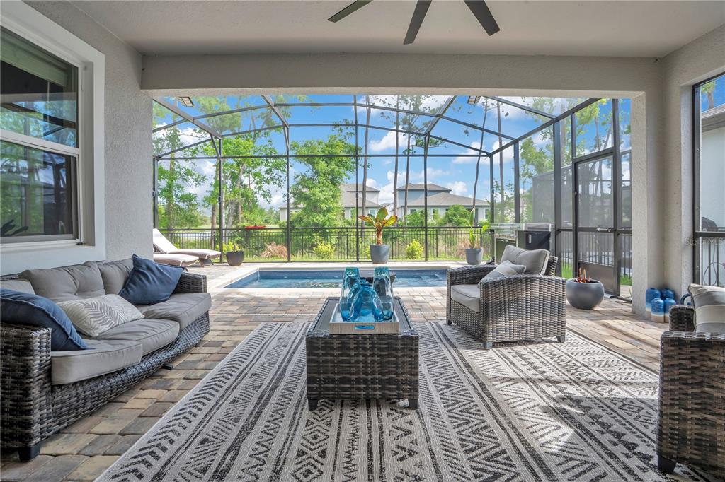 A covered patio features wicker furniture, a patterned rug, and a screened-in pool area — 3160 FIRETHORN CIRCLE, DAYTONA BEACH, FL