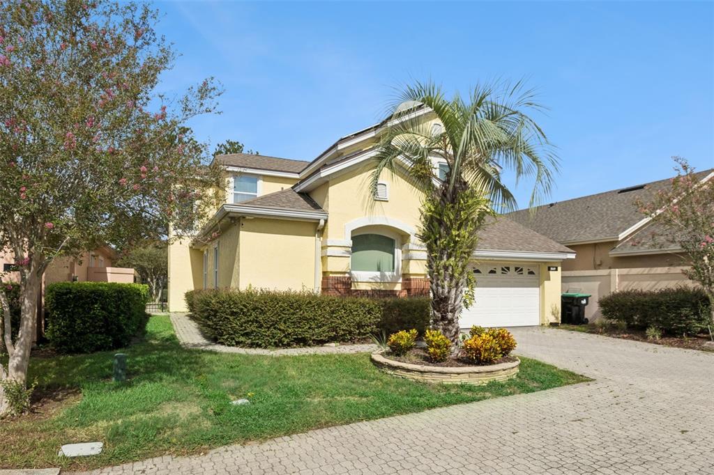 A yellow two-story house with a paved driveway, a palm tree, and a hedge — 2619 WINDCHIME COURT, ORLANDO, FL