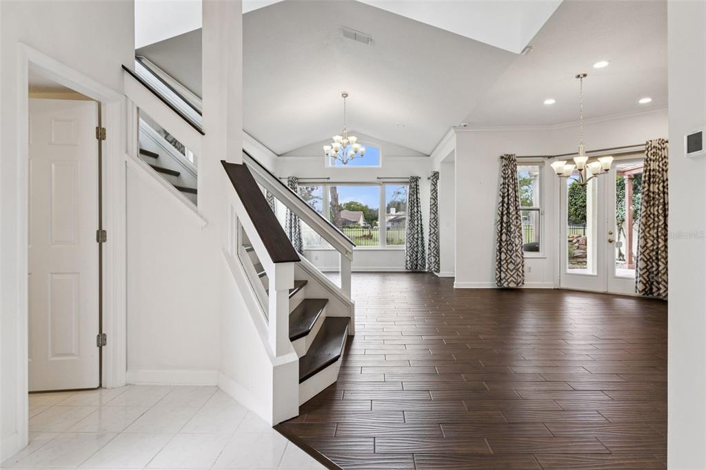 A bright living area features a staircase, vaulted ceilings, and dark wood-look tile flooring — 2619 WINDCHIME COURT, ORLANDO, FL