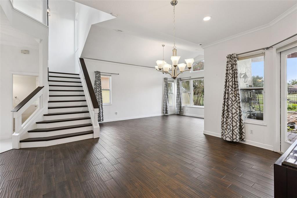 An open living area features dark wood-look tile flooring, a staircase, and a large chandelier — 2619 WINDCHIME COURT, ORLANDO, FL