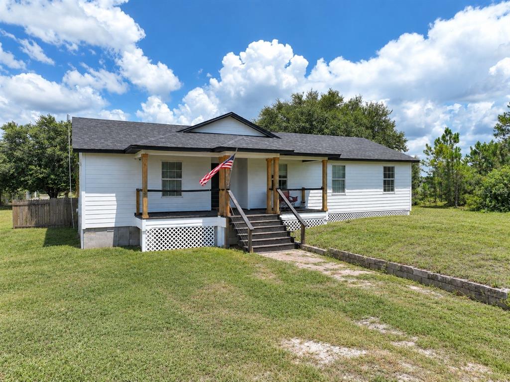 A white, single-story house with a dark roof and a front porch with wooden posts — 1416 WELLS AVENUE, LEHIGH ACRES, FL