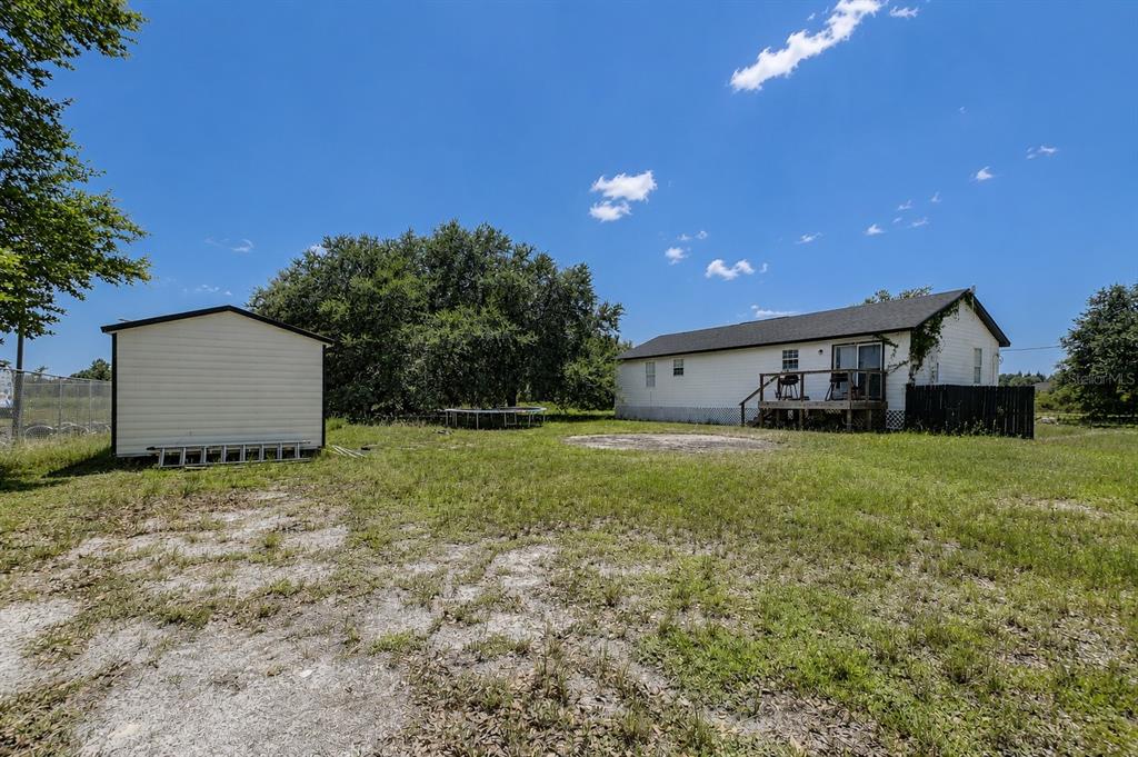 A white house and a detached shed sit on a large, grassy, fenced lot — 1416 WELLS AVENUE, LEHIGH ACRES, FL