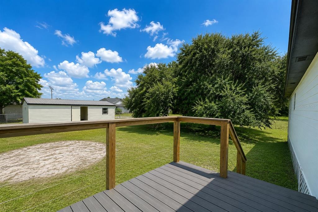 A wooden deck with cable railings overlooks a grassy backyard with a storage shed — 1416 WELLS AVENUE, LEHIGH ACRES, FL
