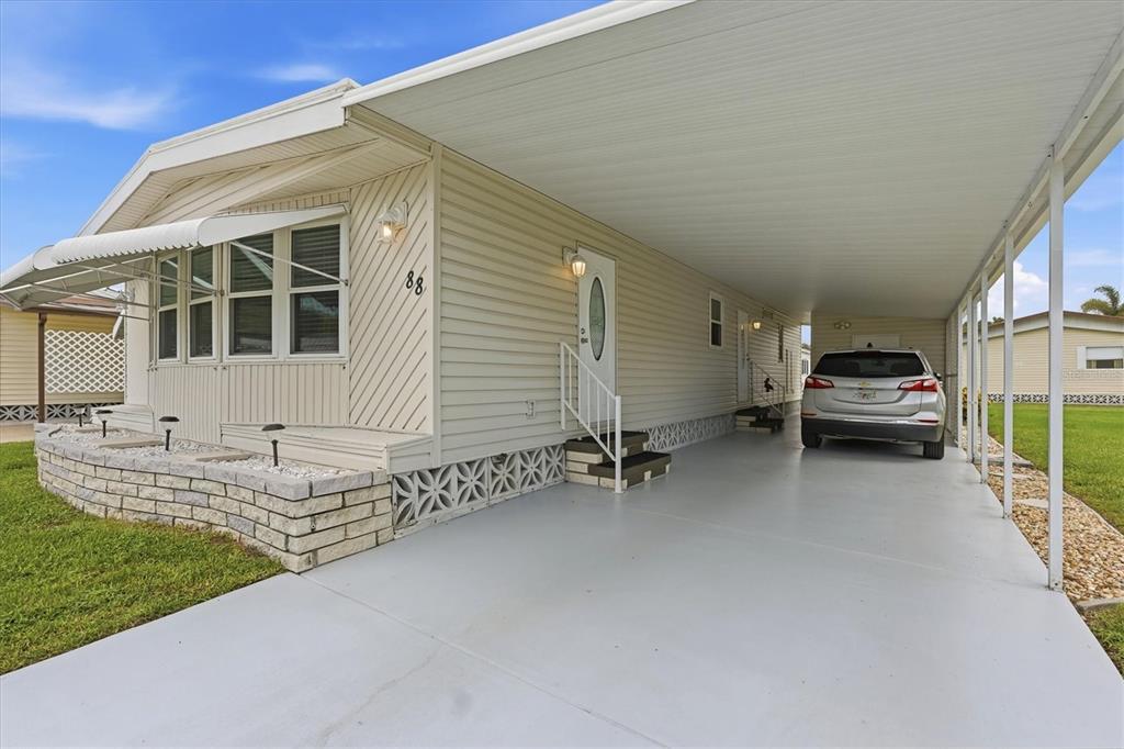 A light-colored mobile home features a large carport and a stone-accented front garden bed — 808 53RD AVENUE E UNIT 88, BRADENTON, FL