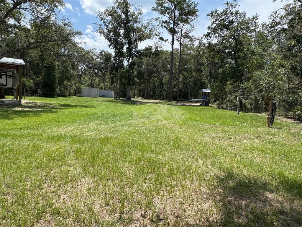 A grassy yard features mature trees, a covered structure, and a shipping container in the distance — 1551 NE 930TH STREET, OLD TOWN, FL