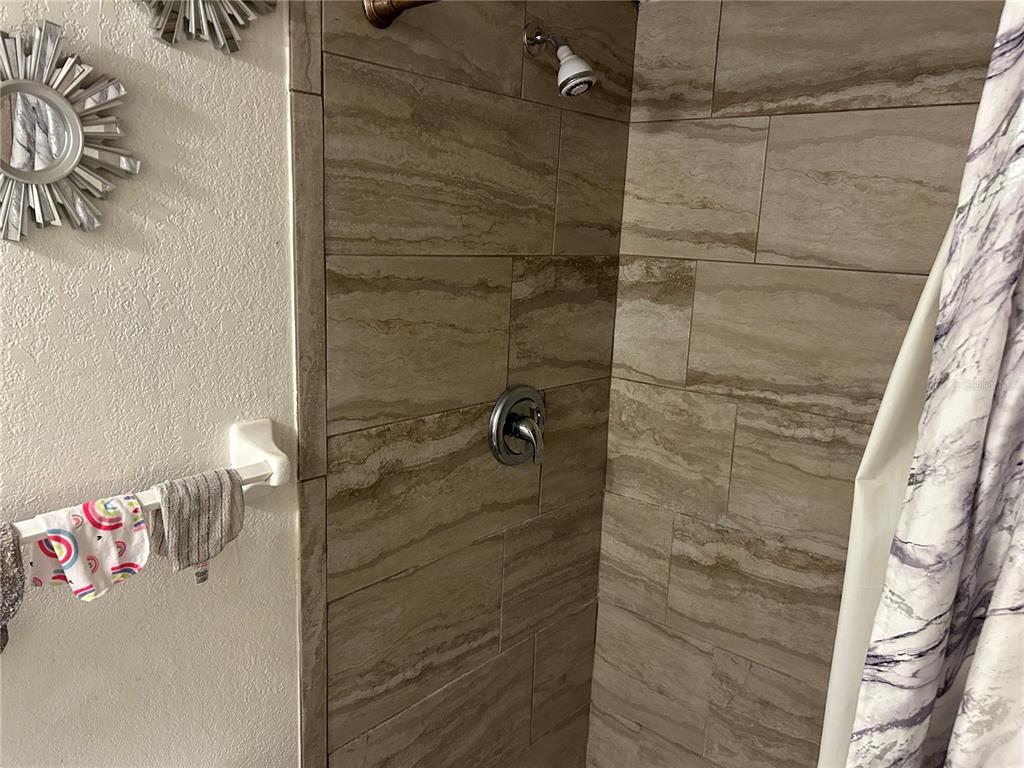 A tiled shower stall with a chrome showerhead and handle next to a towel rack — 6301 58TH STREET N UNIT 505, PINELLAS PARK, FL