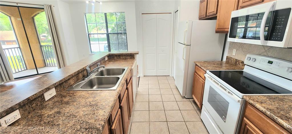 A kitchen features brown laminate countertops, white appliances, and a double sink — 6171 METROWEST BOULEVARD UNIT 107, ORLANDO, FL