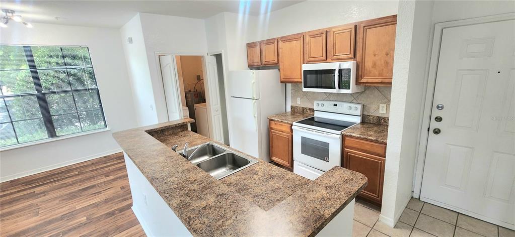 A kitchen features wood cabinets, laminate countertops, white appliances, and a breakfast bar — 6171 METROWEST BOULEVARD UNIT 107, ORLANDO, FL