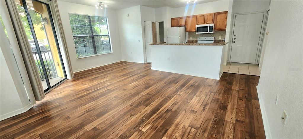 An open-concept living area features wood-look flooring, a kitchen with wood cabinets, and a sliding door — 6171 METROWEST BOULEVARD UNIT 107, ORLANDO, FL