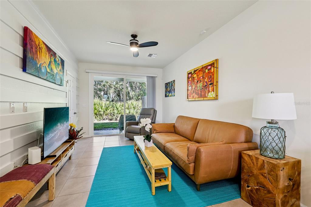 A living room features a tan leather sofa, a turquoise rug, and a sliding glass door — 70 WHISPERING BROOK DRIVE, ST AUGUSTINE, FL