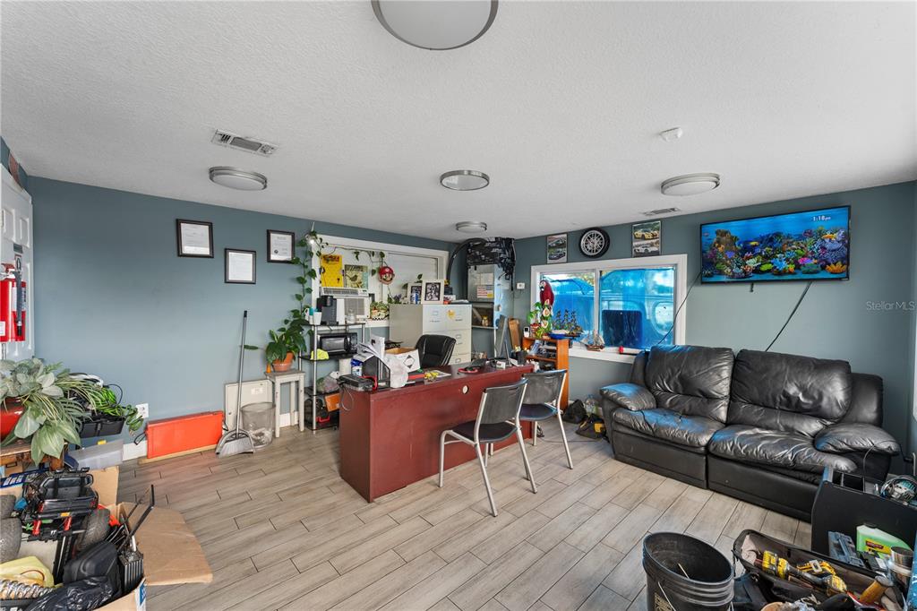 A home office features a desk, black leather sofa, wall-mounted television, and wood-look tile flooring — 5712 15TH STREET E, BRADENTON, FL