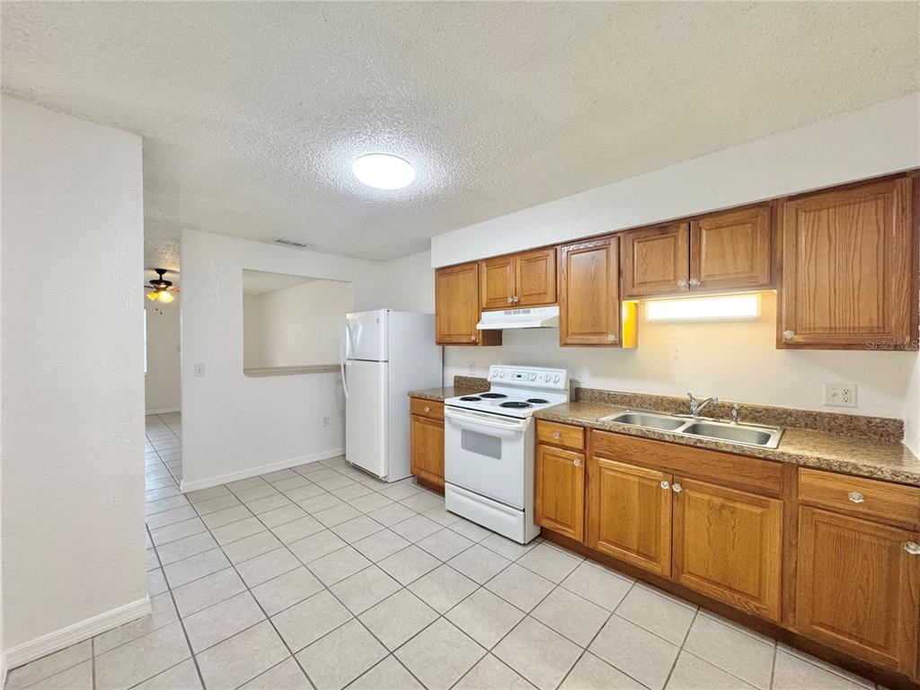 A kitchen features oak cabinets, white appliances, a double sink, and light-colored tile flooring — 2559 ELM AVENUE, LAKE WALES, FL
