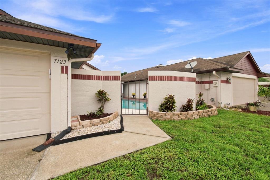 A view of a house exterior featuring a gated courtyard entrance with a swimming pool — 7123 SILVERMILL DRIVE, TAMPA, FL
