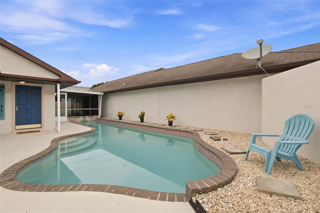 A backyard swimming pool with a brick border sits next to a house and patio — 7123 SILVERMILL DRIVE, TAMPA, FL