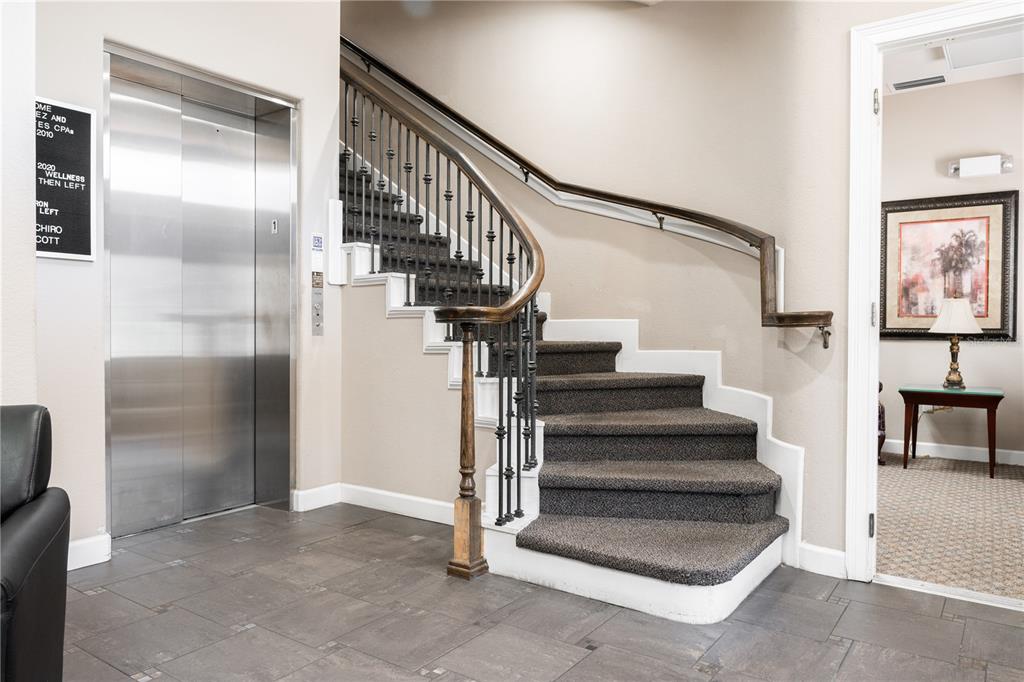 A carpeted staircase with a metal railing sits beside a stainless steel elevator in a lobby — 1100 TOWN PLAZA COURT UNIT 2010-F, WINTER SPRINGS, FL