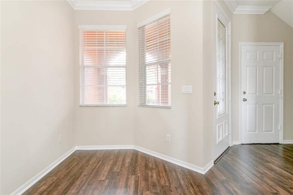 An empty room with wood-look flooring, two windows with blinds, and a white entry door — 9426 SILVER BUTTONWOOD STREET, ORLANDO, FL
