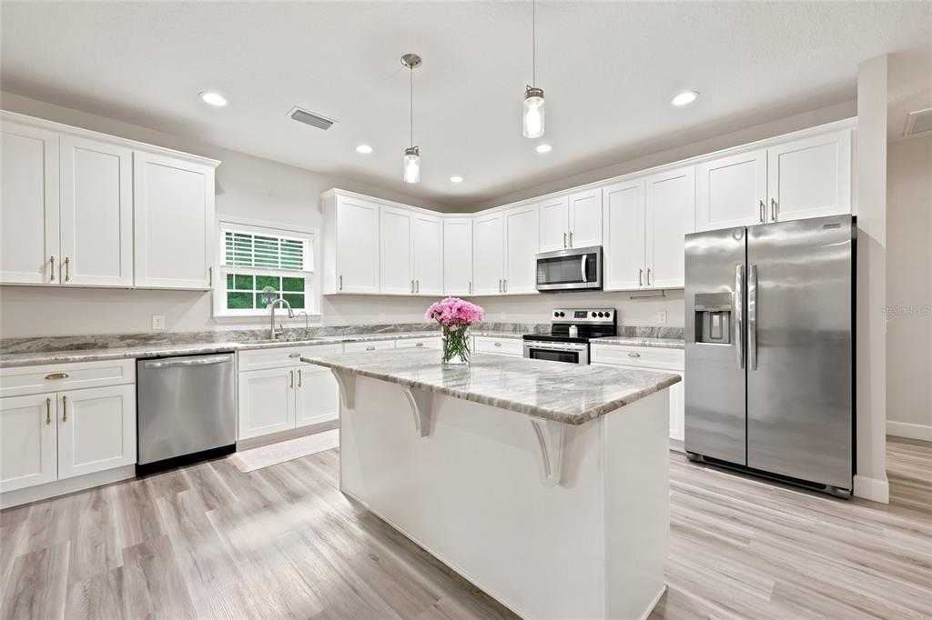 A kitchen features white cabinets, stainless steel appliances, a marble-topped island, and light wood flooring — 5766 SW COUNTY ROAD 18, FORT WHITE, FL