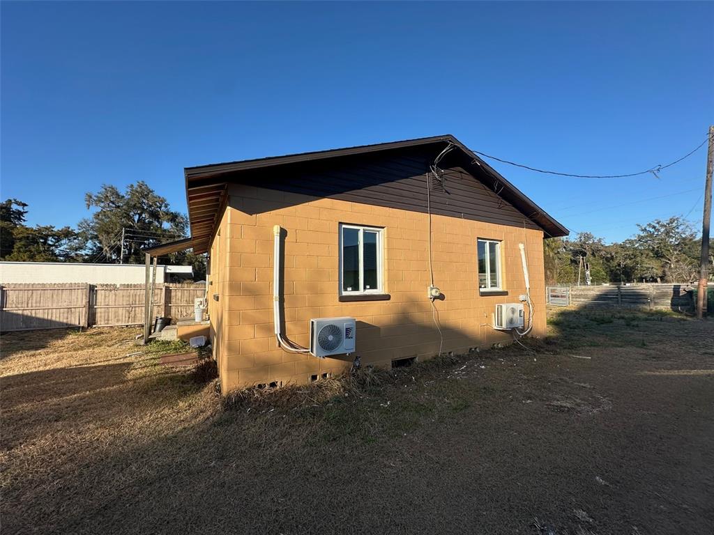 The exterior of a tan concrete block house features two windows and two wall-mounted AC units — 9710 NE 21ST AVENUE, ANTHONY, FL
