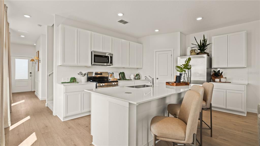 A modern kitchen features white cabinetry, quartz countertops, a center island, and stainless steel appliances — 3116 ROCKWOOD WAY, MINNEOLA, FL