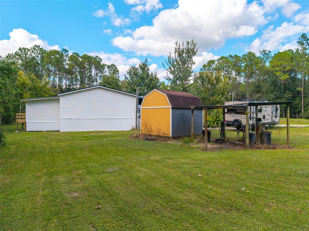 An exterior view of a white mobile home with a metal-roofed porch and wooden stairs — 17822 COMMONWEALTH AVENUE N, POLK CITY, FL
