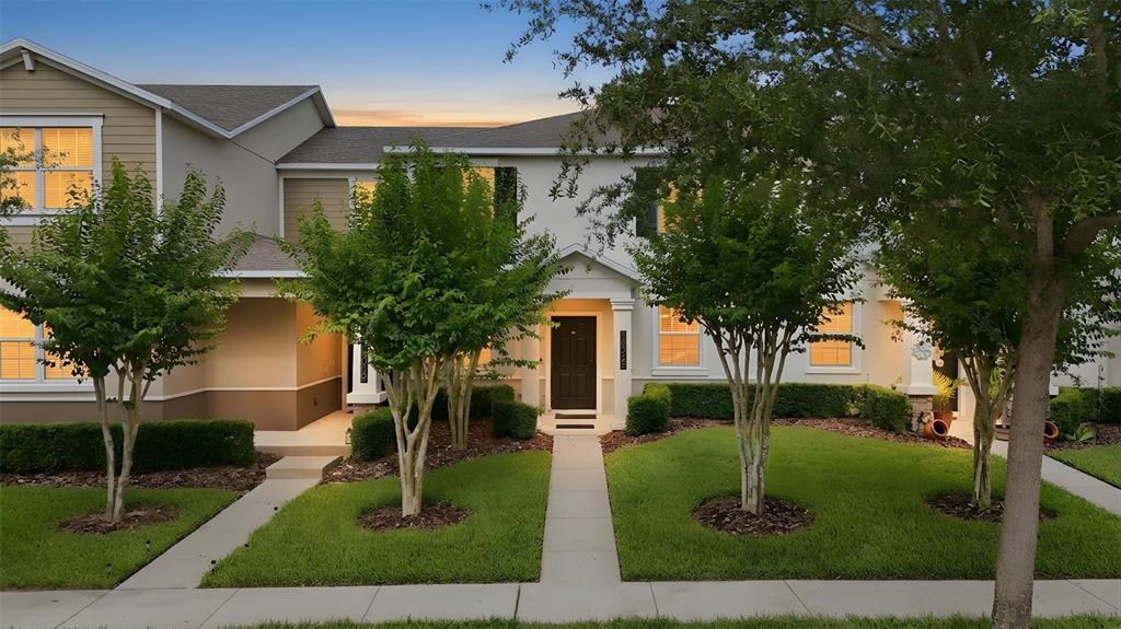 A two-story townhouse exterior features a dark front door, manicured lawn, and several small trees — 11025 SUSPENSE DRIVE, WINTER GARDEN, FL
