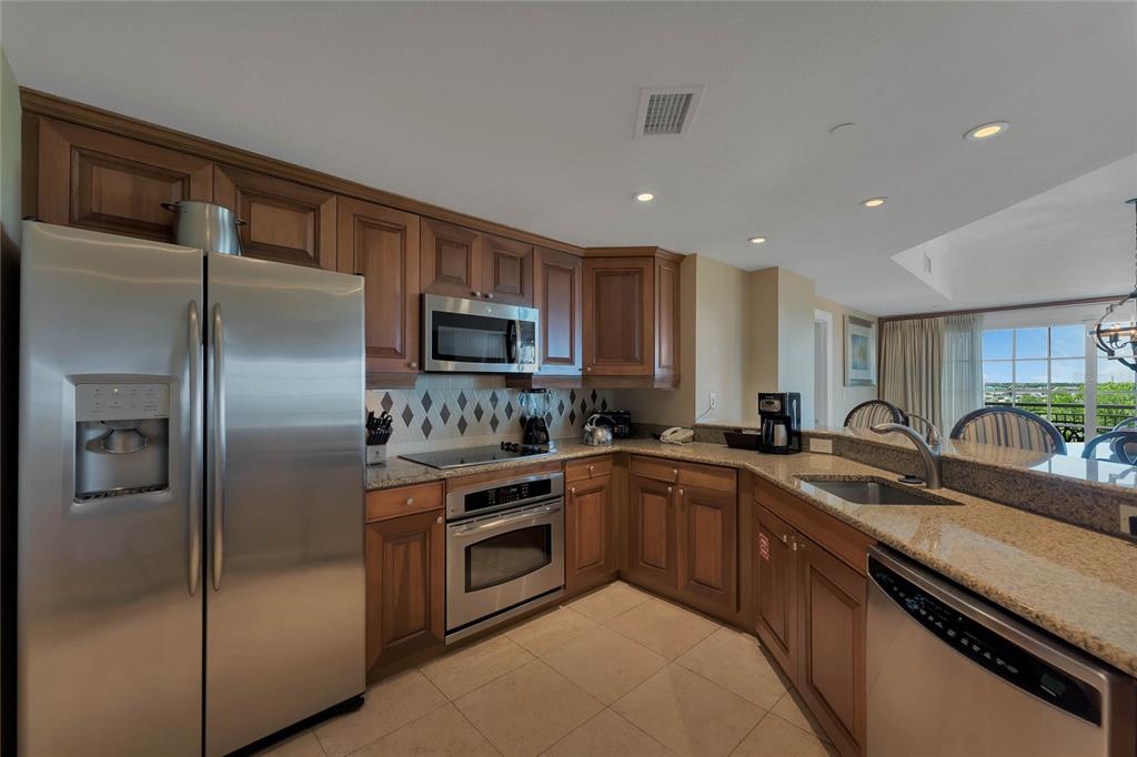 A kitchen with wood cabinets, stainless steel appliances, granite countertops, and a tile floor — 7593 GATHERING DRIVE UNIT 309, REUNION, FL