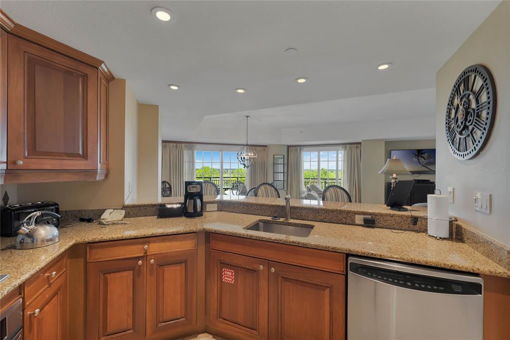 A kitchen with wood cabinets, granite countertops, and a sink overlooks a bright living area — 7593 GATHERING DRIVE UNIT 309, REUNION, FL