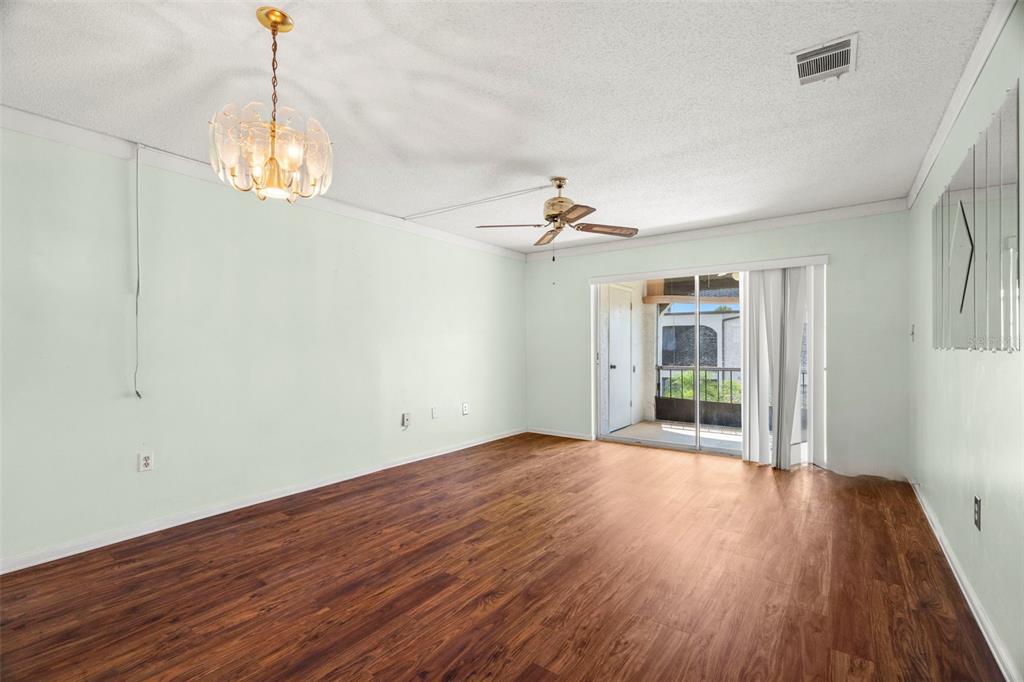 An empty living room with wood-look flooring, a ceiling fan, a chandelier, and sliding doors — 7701 STARKEY ROAD UNIT 504, SEMINOLE, FL
