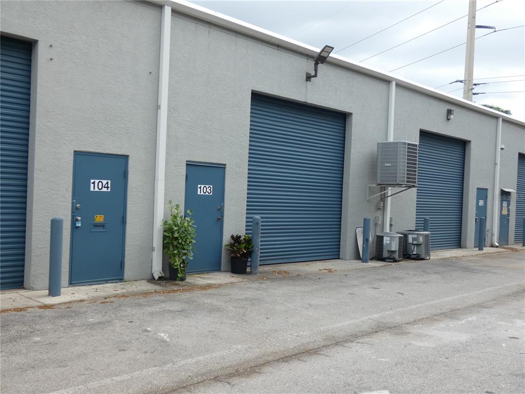 The exterior of a commercial building features multiple blue roll-up doors and numbered entry doors — 1882 PORTER LAKE DRIVE UNIT 103, SARASOTA, FL