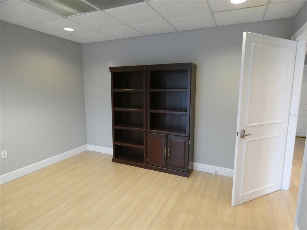 A room with light wood flooring, gray walls, a drop ceiling, and a dark wooden bookcase — 1882 PORTER LAKE DRIVE UNIT 103, SARASOTA, FL
