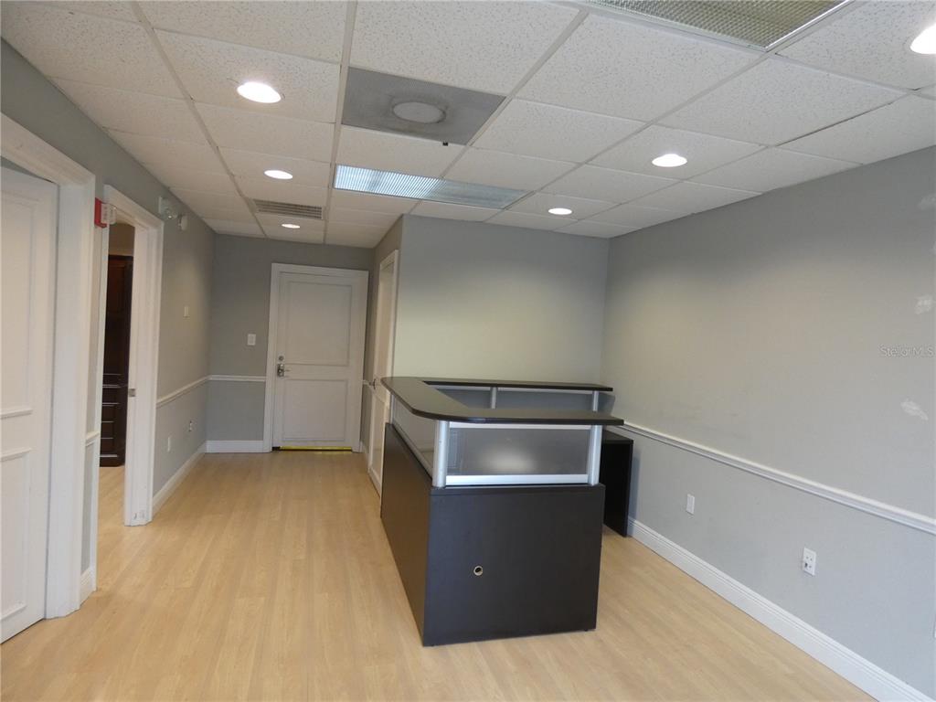 An office reception area features light wood flooring, gray walls, and a dark reception desk — 1882 PORTER LAKE DRIVE UNIT 103, SARASOTA, FL