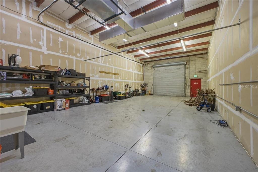 An industrial warehouse space with concrete floors, exposed steel beams, and a roll-up garage door — 1882 PORTER LAKE DRIVE UNIT 103, SARASOTA, FL
