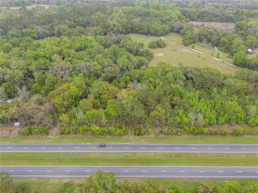 An aerial view shows a wooded lot bordering a multi-lane highway and open pasture — 17819 SR-25, MICANOPY, FL