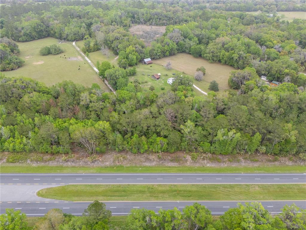 An aerial view shows a rural property with several buildings, pastures, and trees near a highway — 17819 SR-25, MICANOPY, FL