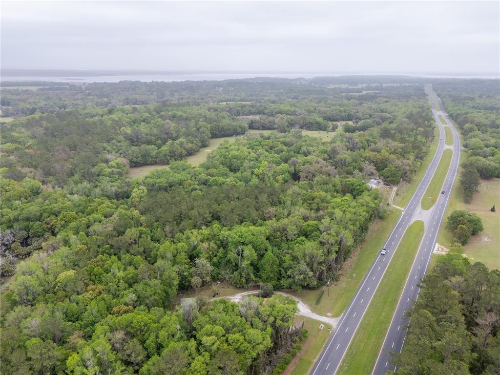 An aerial view shows a wooded lot adjacent to a divided highway — 17819 SR-25, MICANOPY, FL