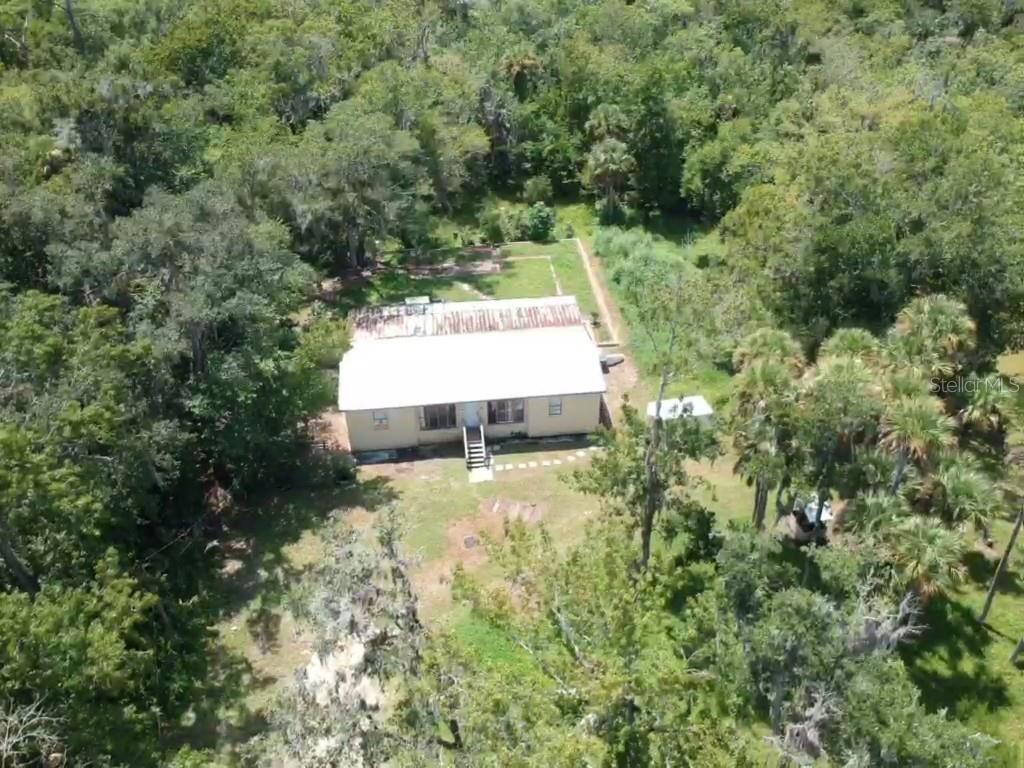 An aerial view shows a single-story house with a metal roof surrounded by dense woods — 1550 BOYCE CIRCLE, EDGEWATER, FL
