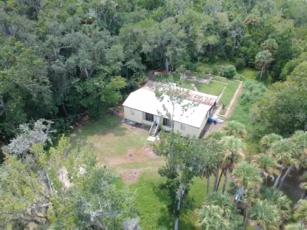 An aerial view shows a single-story house with a metal roof surrounded by dense trees — 1550 BOYCE CIRCLE, EDGEWATER, FL