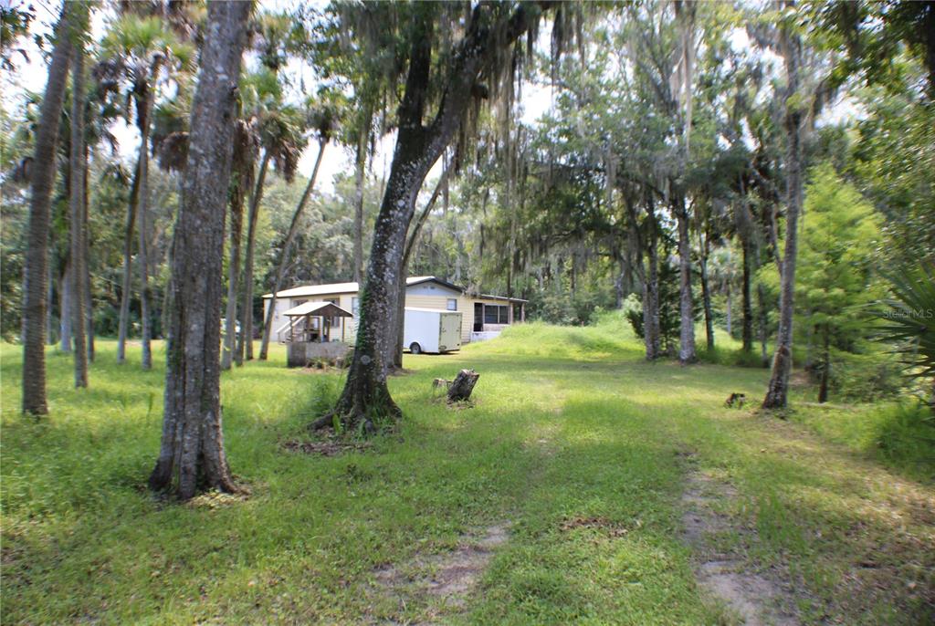 A single-story house sits in a grassy, wooded lot with a small trailer parked nearby — 1550 BOYCE CIRCLE, EDGEWATER, FL