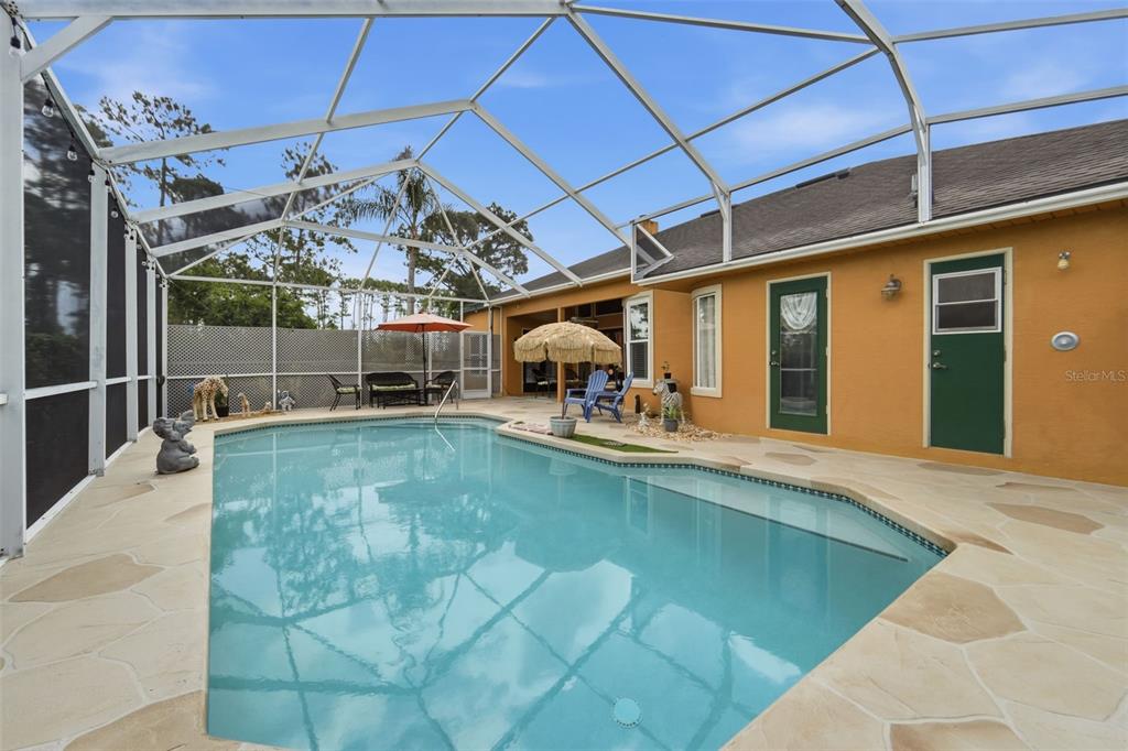 A screened-in swimming pool area with a beige stone deck and a yellow exterior wall — 102 BIRKWOOD COURT, DEBARY, FL