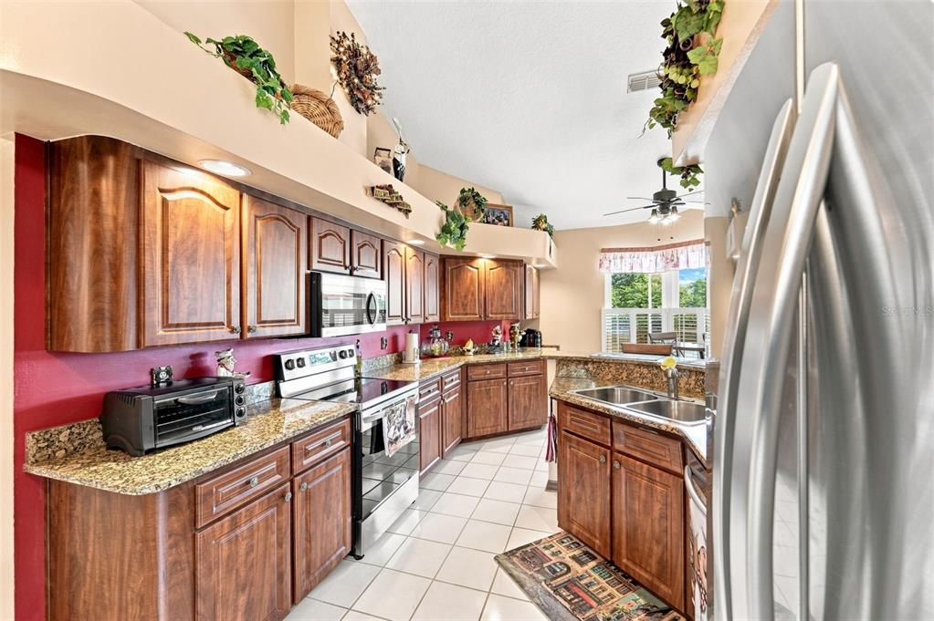 A kitchen features wood cabinets, granite countertops, white tile floors, and a red accent wall — 102 BIRKWOOD COURT, DEBARY, FL