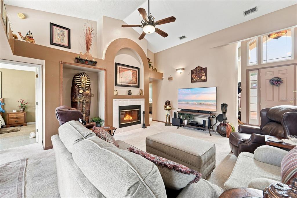 A living room features a fireplace, vaulted ceiling, Egyptian-themed decor, and beige carpeting — 102 BIRKWOOD COURT, DEBARY, FL