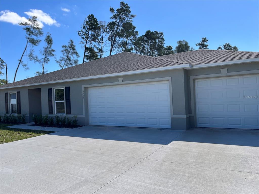 A single-story house exterior features a two-car garage, a concrete driveway, and gray siding — 3402 SW 165TH LOOP, OCALA, FL