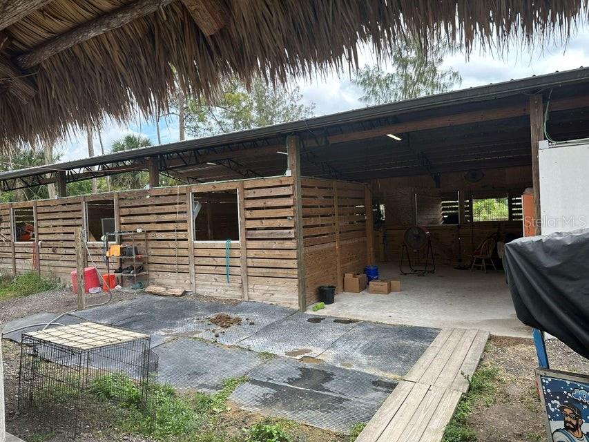 An outdoor horse stable with wooden stalls, a concrete floor, and a thatched roof overhang — 3525 D RD, LOXAHATCHEE GROVES, FL
