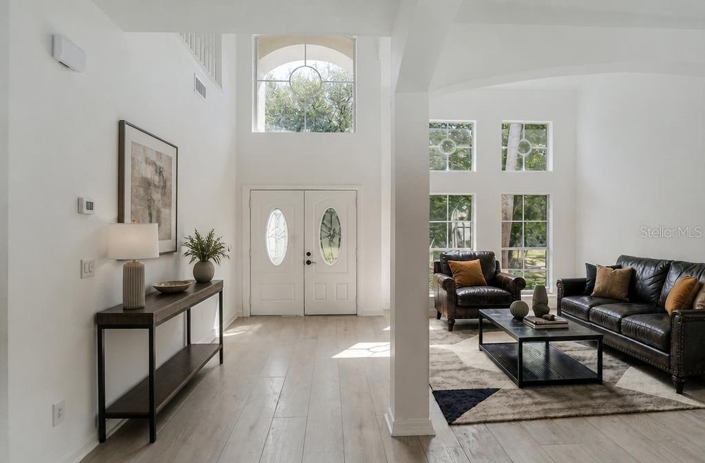 A bright entryway with light wood floors leads into a living room with dark leather furniture — 14927 FAVERSHAM CIRCLE, ORLANDO, FL