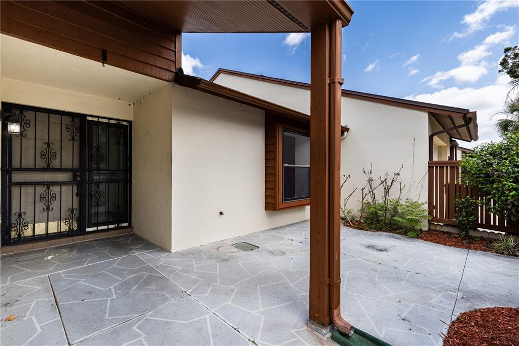 A concrete patio features a decorative pattern, a metal screen door, and brown trim — 2681 WASHINGTON AVENUE UNIT 18, EUSTIS, FL