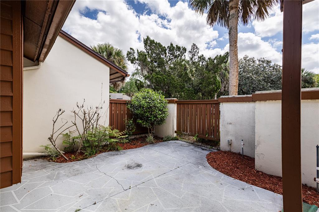 A concrete patio area features a wooden privacy fence, landscaping, and a white exterior wall — 2681 WASHINGTON AVENUE UNIT 18, EUSTIS, FL