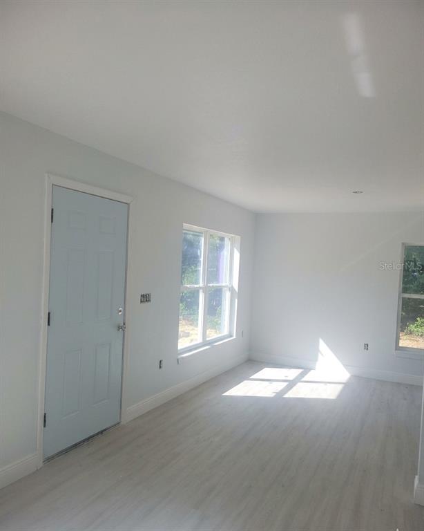 A bright room features light-colored wood-look flooring, white walls, and a light blue door — 79 NE 156TH COURT, WILLISTON, FL