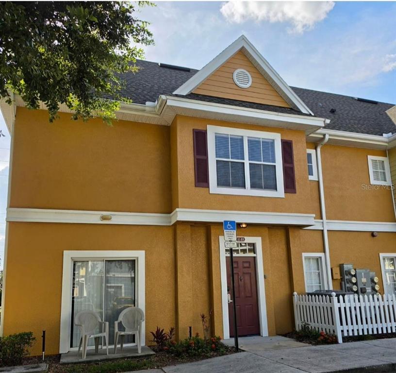 A two-story yellow stucco townhouse features a brown front door and a white picket fence — 2260 SAN VITAL DRIVES UNIT 108, KISSIMMEE, FL