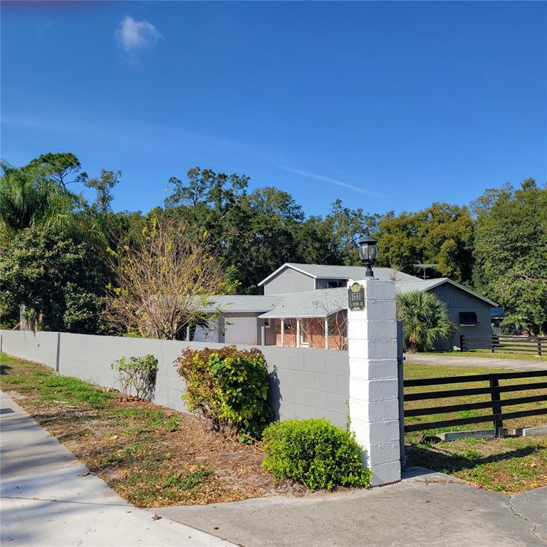 A gray house with a brick accent wall is viewed behind a concrete block wall — 1661 VOTAW ROAD, APOPKA, FL